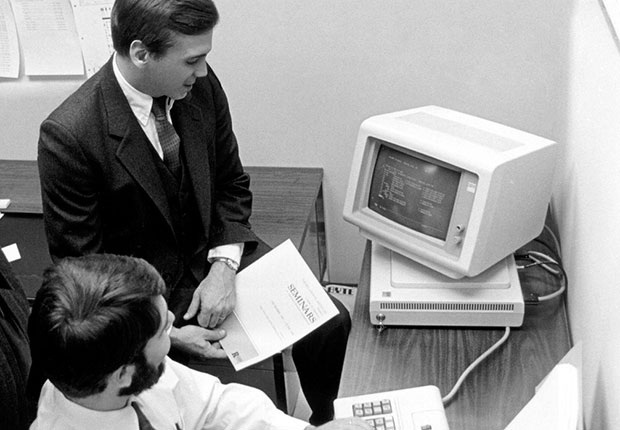 Deux personnes en costume autour d'un ancien modèle d'ordinateur
