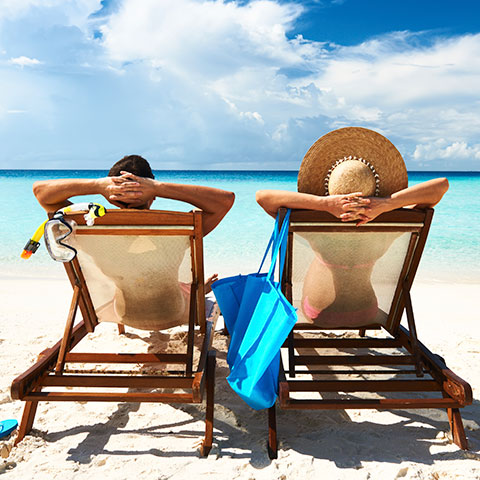 Un couple, vu de dos, allongé sur des transats sur une plage paradisiaque