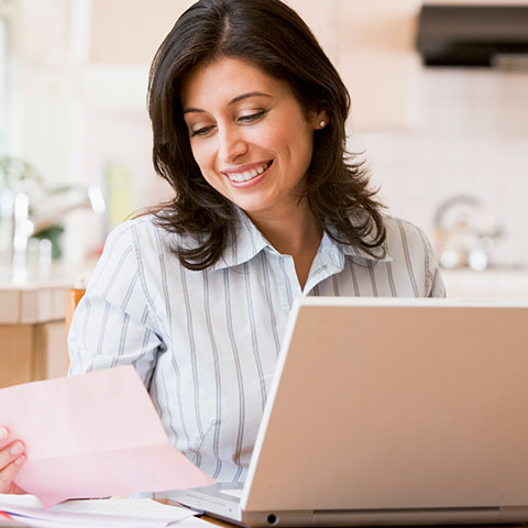 Femme avec un ordinateur portable regardant en souriant un document papier